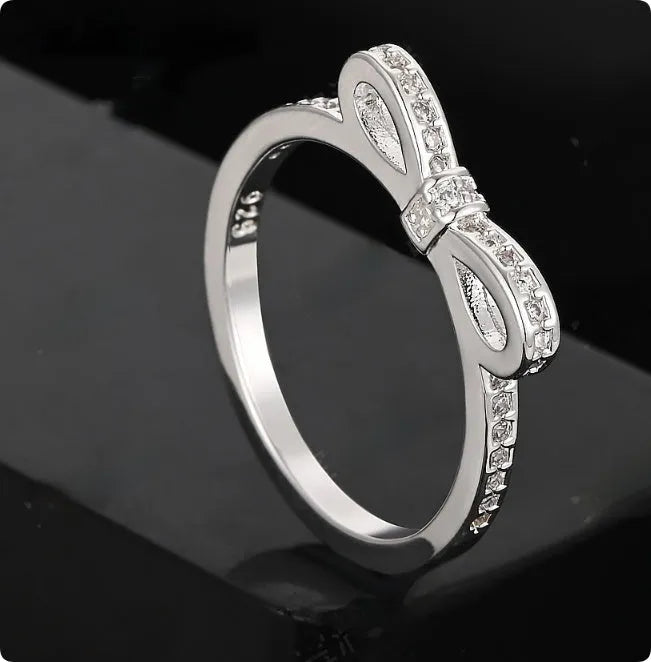 Close-up of a silver-tone bow-shaped ring with sparkling zircon crystal accents on a hand.