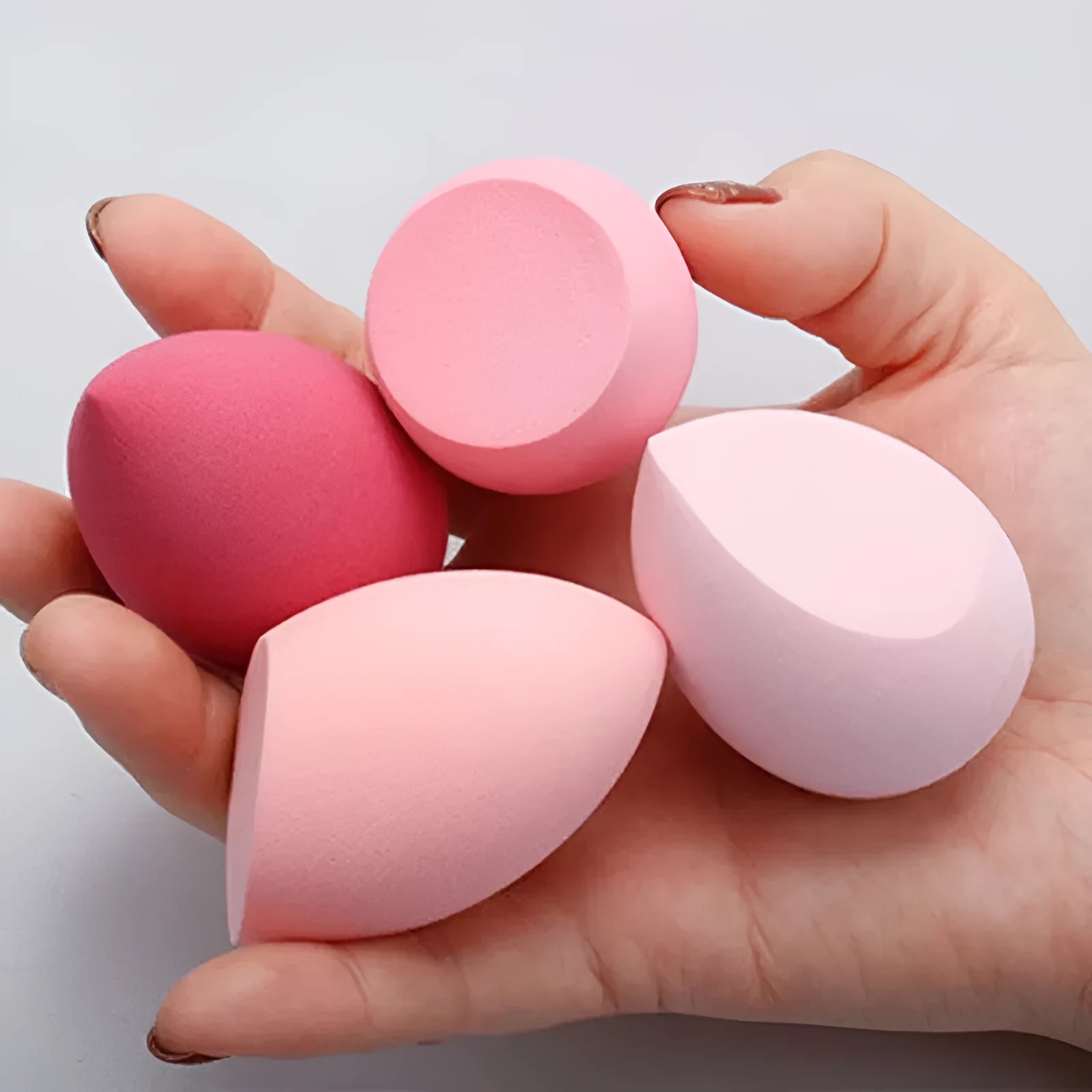 Set of seven coloured makeup sponges in different shapes on a pink background