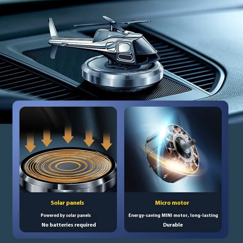 Silver metal solar-powered helicopter car air freshener with spinning blades on a dashboard.