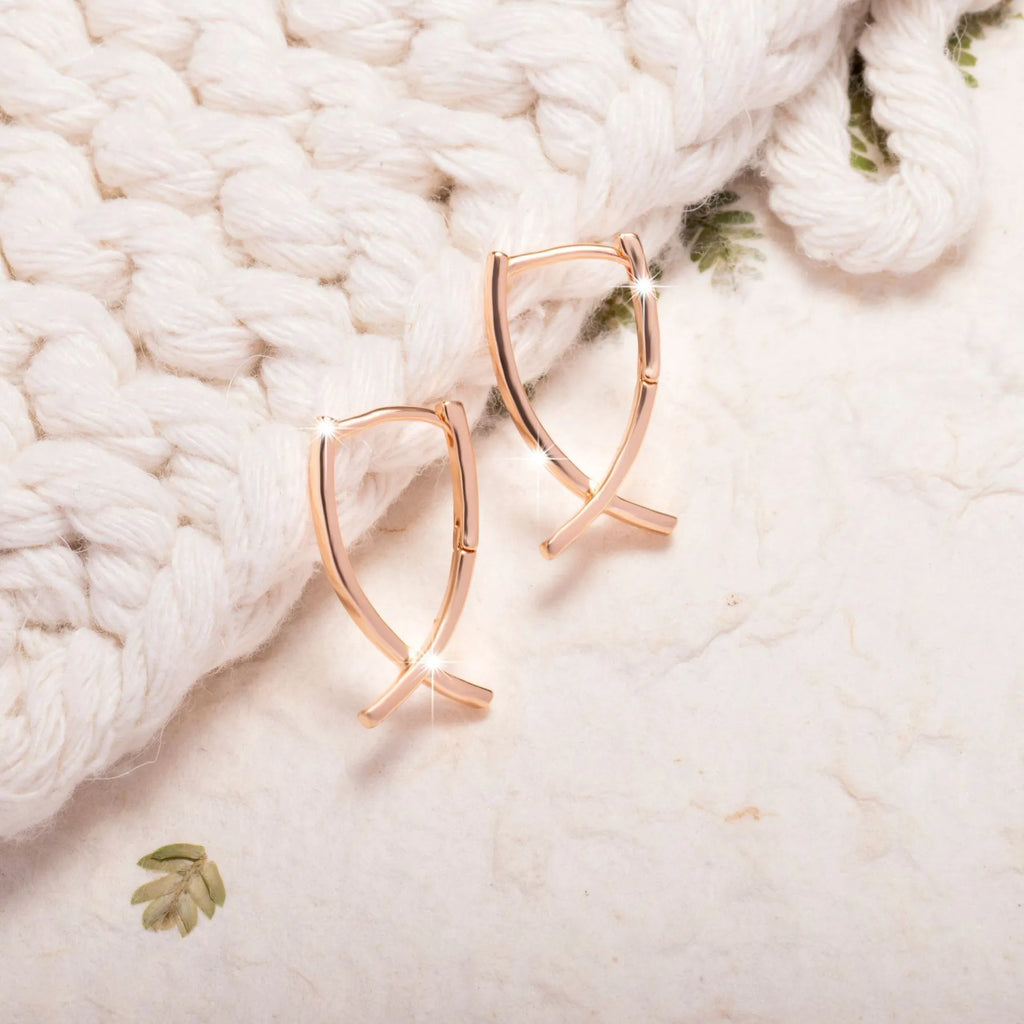 Rose gold tone cross-shaped copper earrings on a flat surface, showing polished finish and push-back clasp.