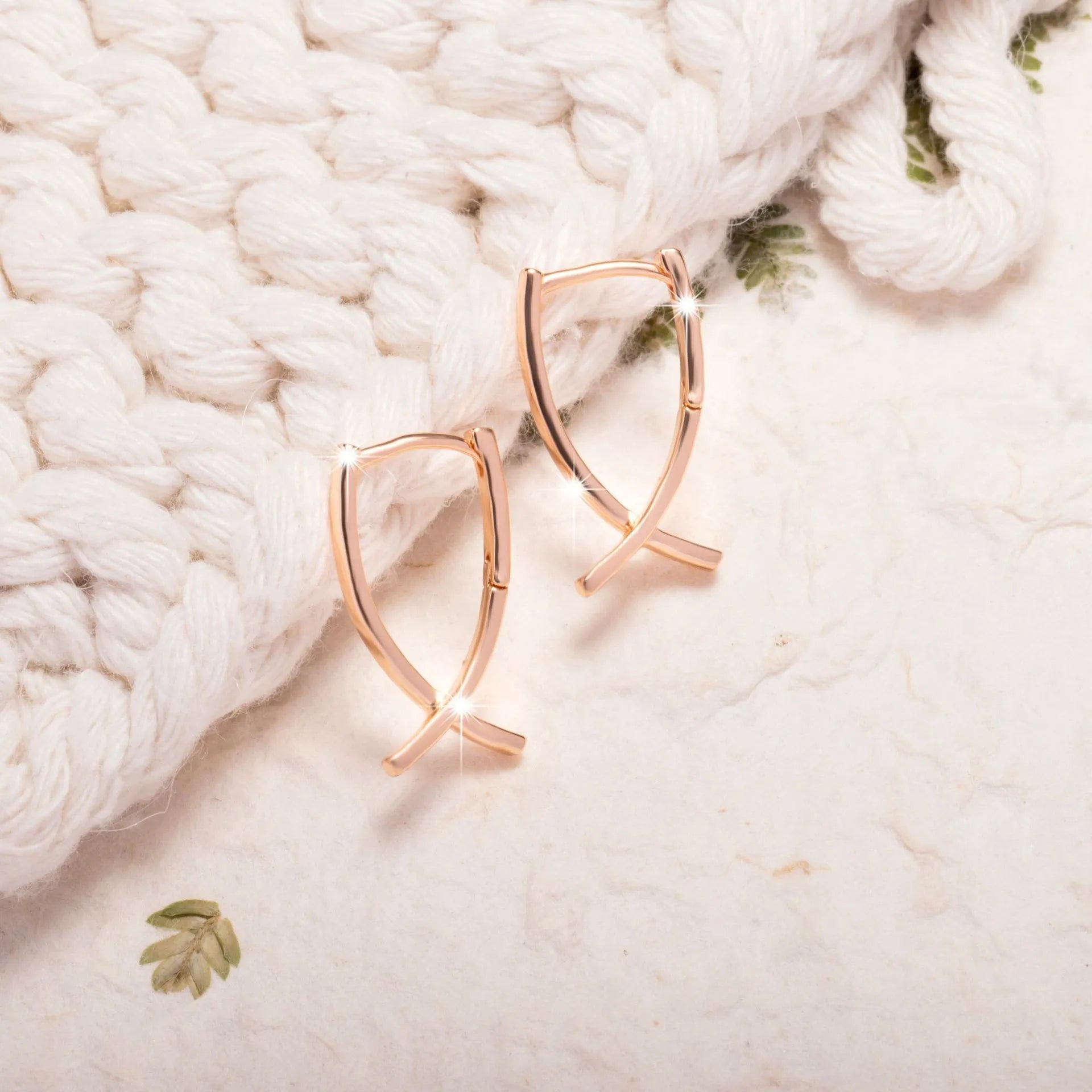 Rose gold tone cross-shaped copper earrings on a flat surface, showing polished finish and push-back clasp.