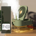 White or green USB desktop fan humidifier with remote control on a wooden desk.