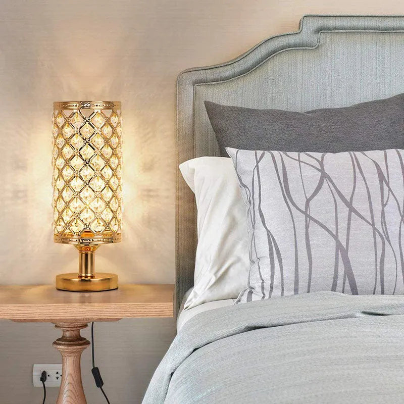 Modern crystal table lamp with gold metal base and hollow-carved crystal shade on a bedside table
