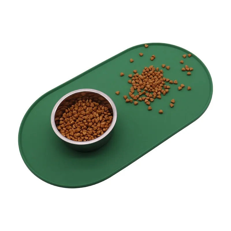 Green silicone cat feeding mat with raised edges containing dry kibble, placed on a wooden floor.