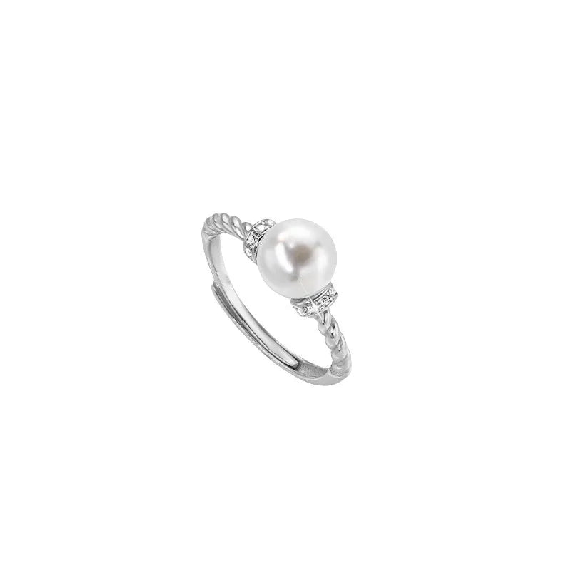 Close-up of an adjustable geometric twist ring in copper with a central pearl inlay, shown on a finger.