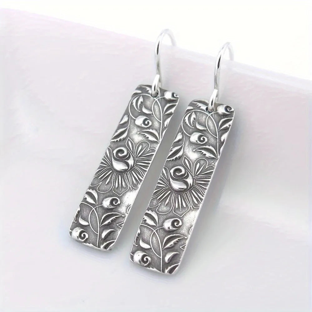 Silver geometric long strip drop earrings with carved vine pattern on a white background.