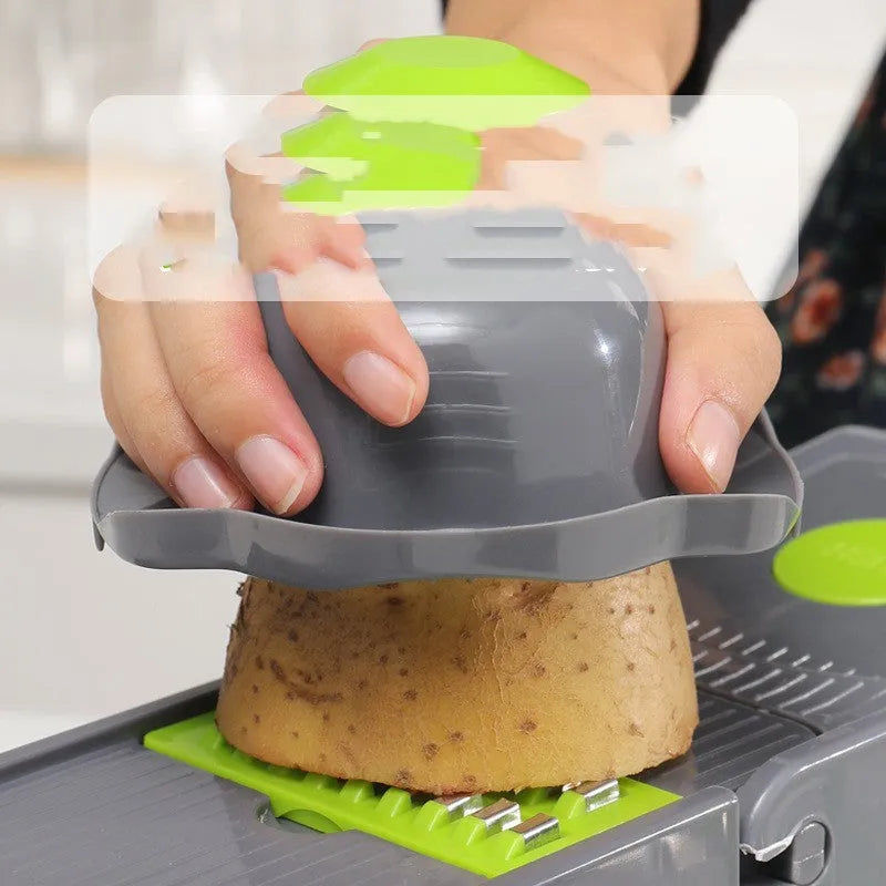 Grey stainless steel vegetable cutter with multiple blades and accessories on kitchen work surface