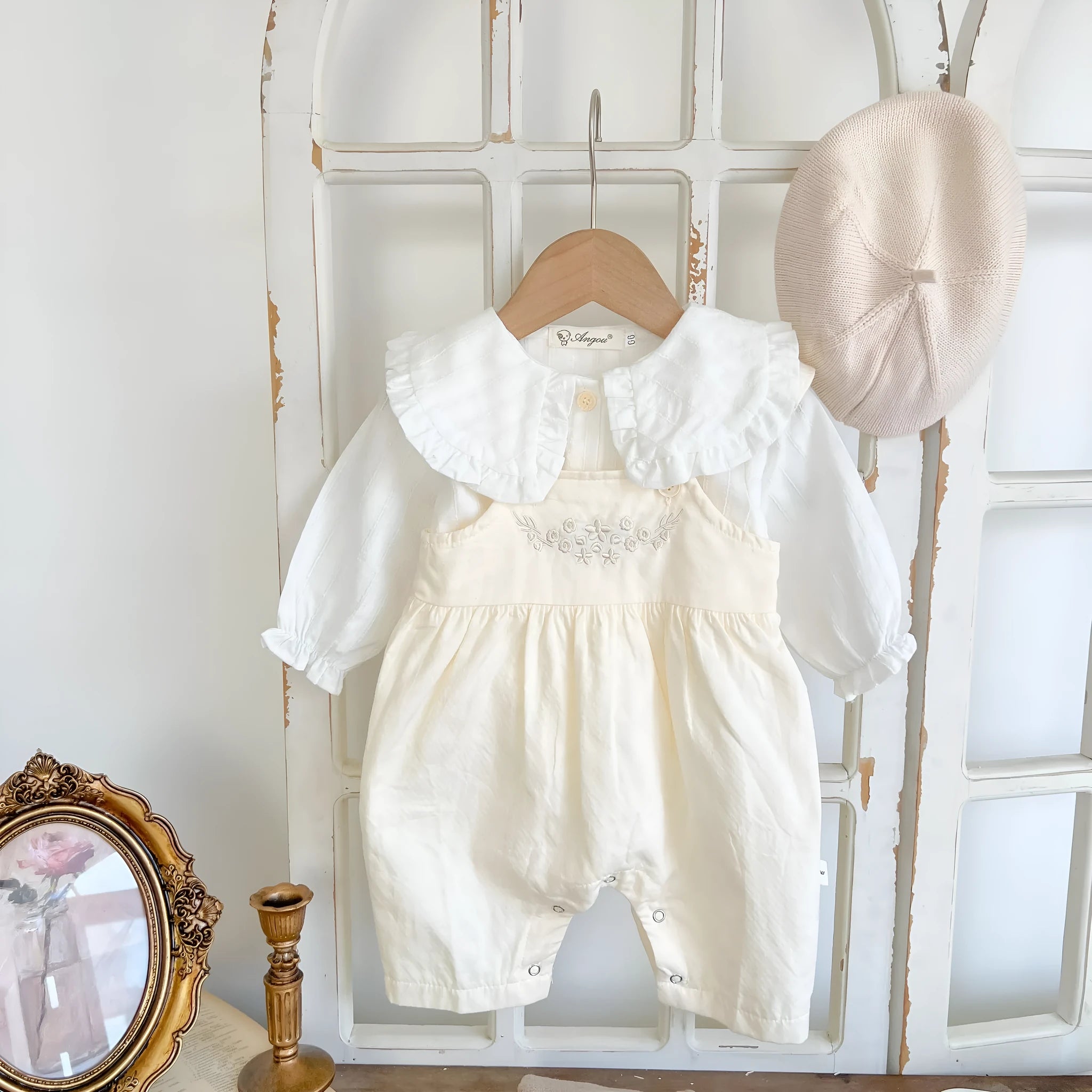Baby girl wearing a loose-fit cotton suspender romper with adjustable straps in an apricot colour.