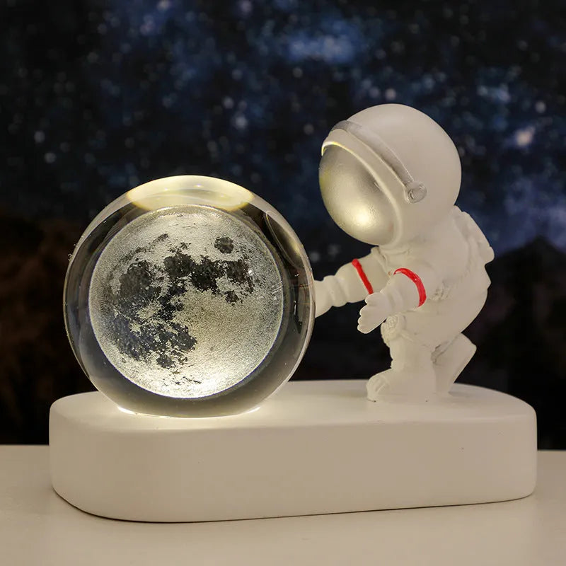 6cm glowing resin crystal ball night light showing an astronaut and planets inside, on a bedside table.