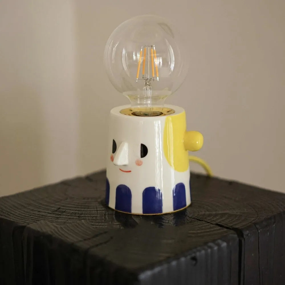 Off-white handmade ceramic table lamp with a rounded shape on a wooden surface.