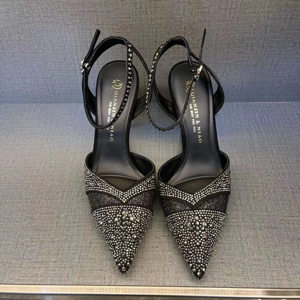 Women's black stiletto high heel with pointed toe and red sole, shown from the side.