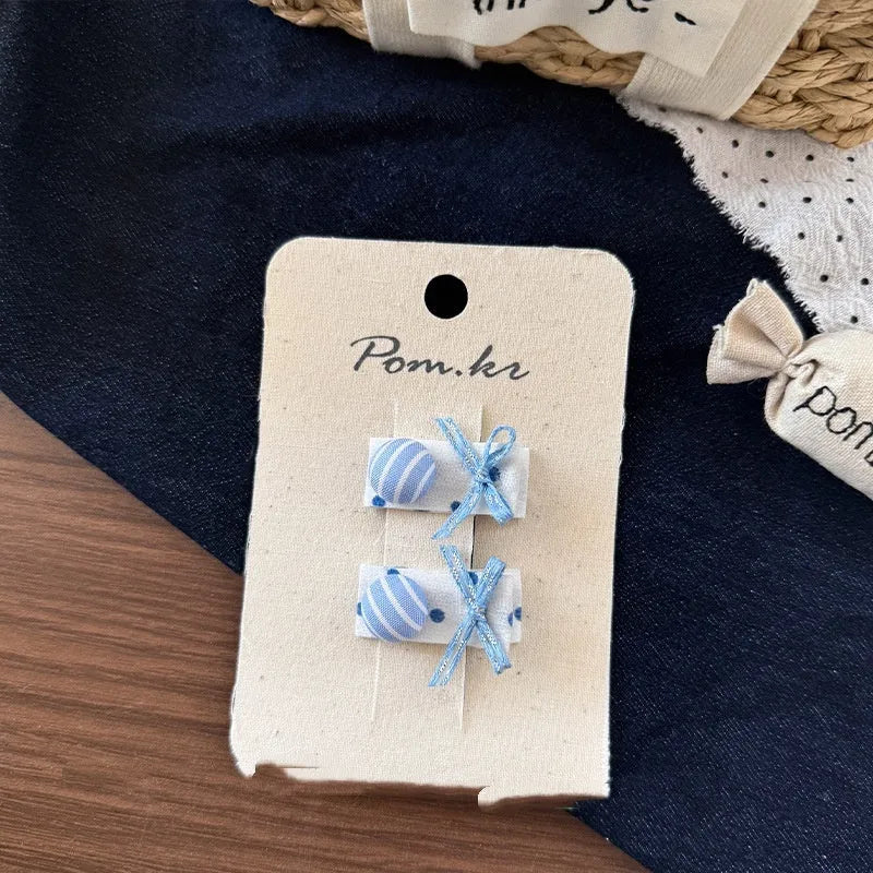 One pair of children's cloth hair clips with bow and flower detailing, shown in a choice of five styles and two clip sizes.