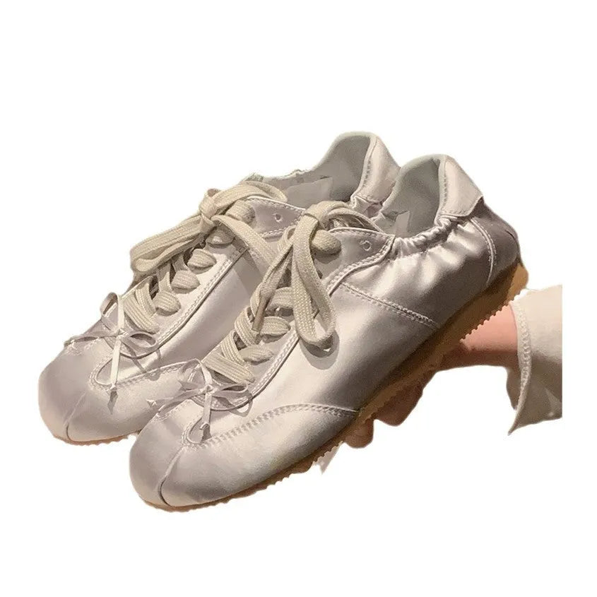 Women's champagne pink satin ballet flats with front lace-up and round toe on a white background.