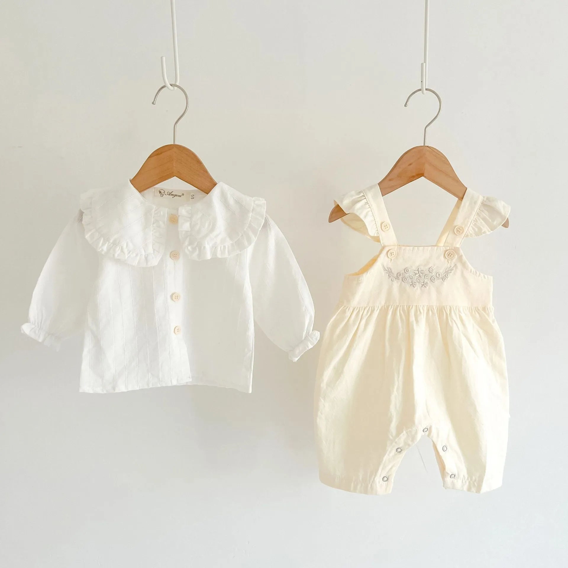Baby girl wearing a loose-fit cotton suspender romper with adjustable straps in an apricot colour.