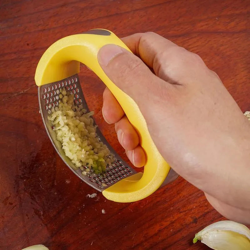 Stainless steel garlic press with coloured ergonomic handle on a kitchen counter.