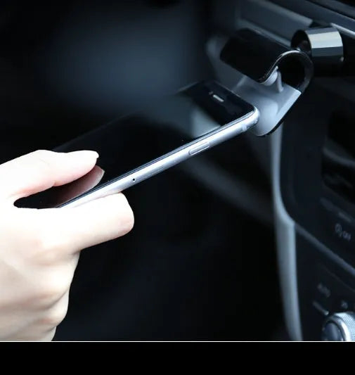 Black universal car phone holder with 360-degree rotating head and adhesive mount on a car dashboard.