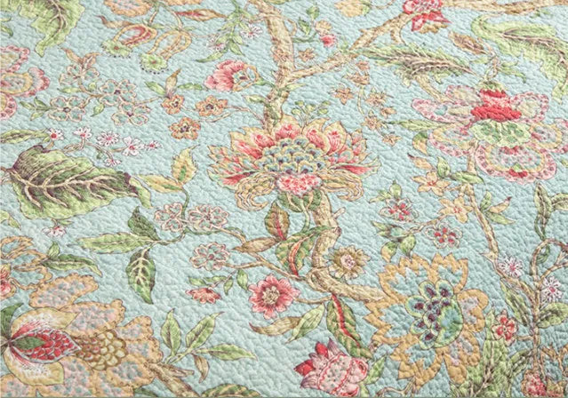 Blue American floral and bird pattern quilted cotton bedspread draped on a double bed
