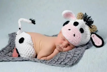 Hand-knitted white baby cow suit with hat and trousers for a newborn.