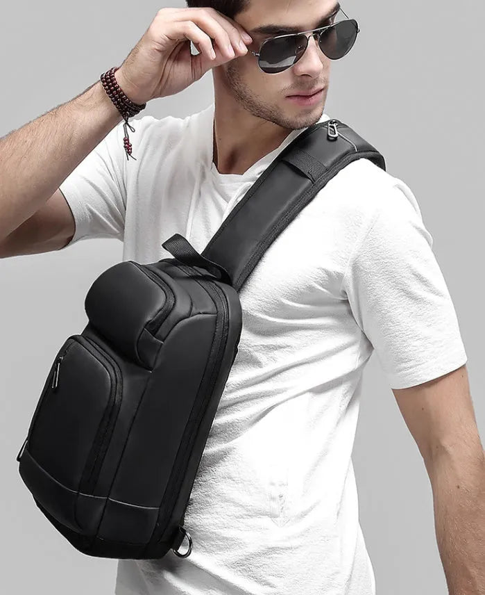 Black square PVC outdoor shoulder bag with an air cushion strap and zipper opening.