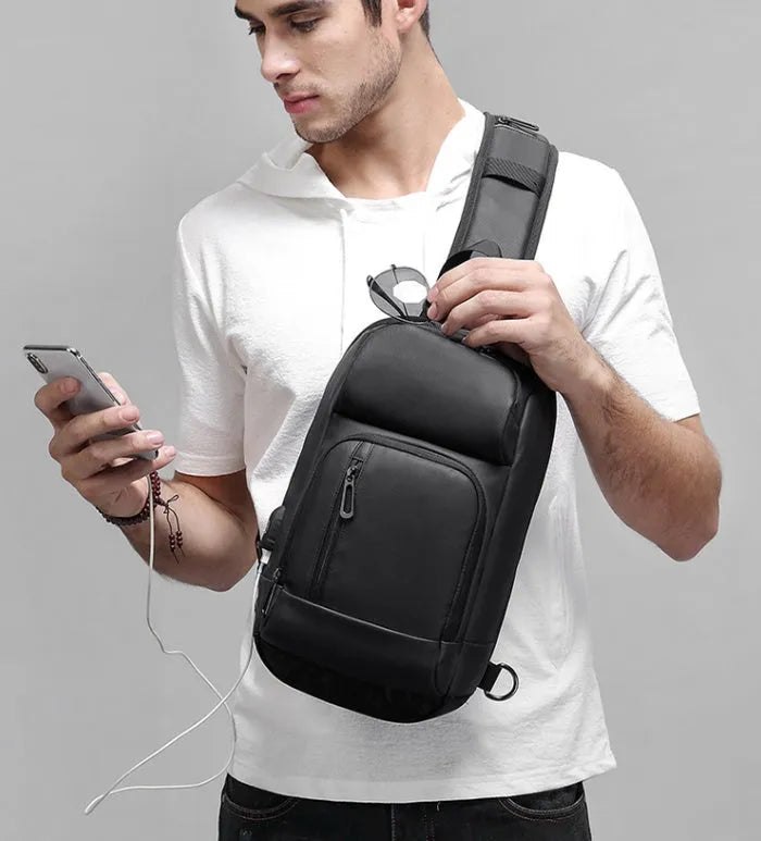 Black square PVC outdoor shoulder bag with an air cushion strap and zipper opening.