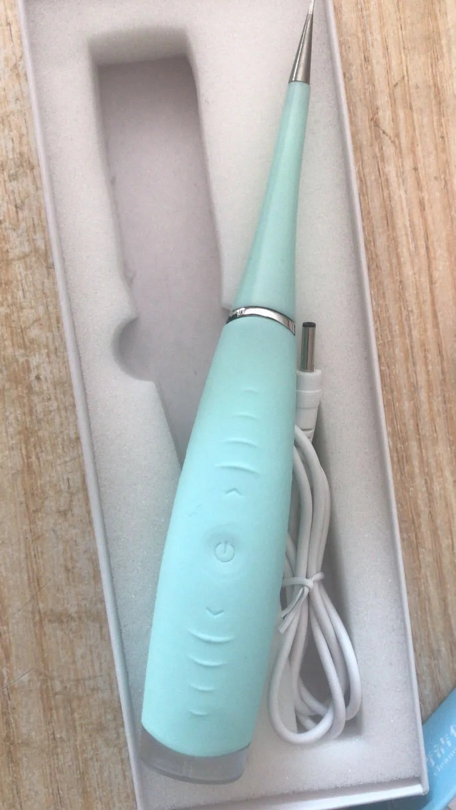 Pink and blue waterproof electric dental scaler with silicone handle and charging cable on a bathroom counter.