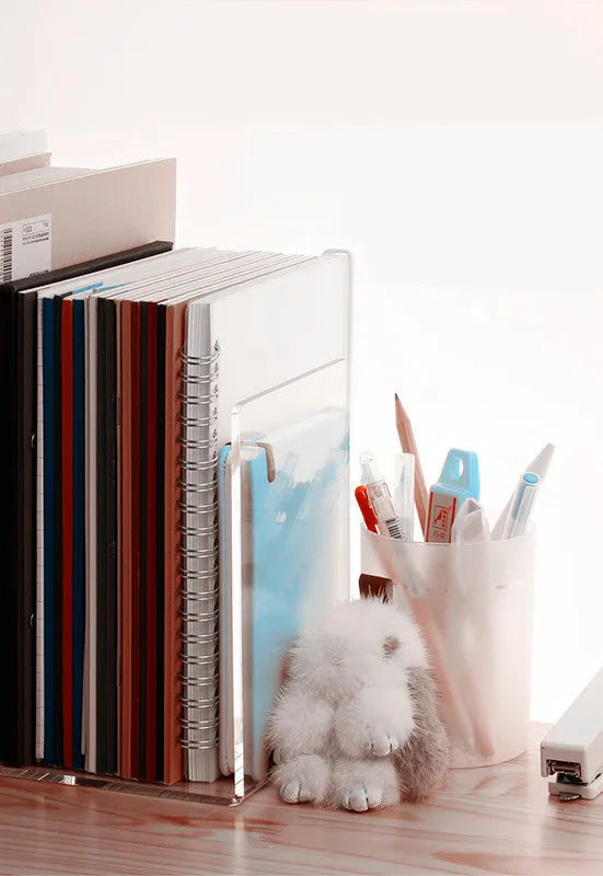 Transparent acrylic bookshelf display rack on a desk holding two books.