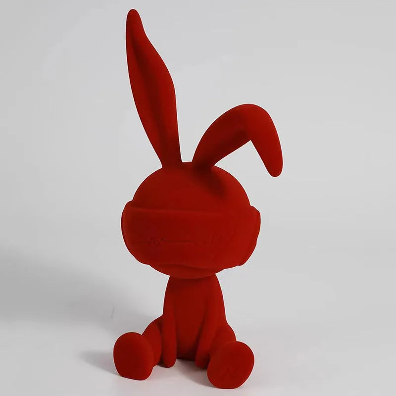 Suede blindfold rabbit resin ornament in blue, green, or red colour on a table.