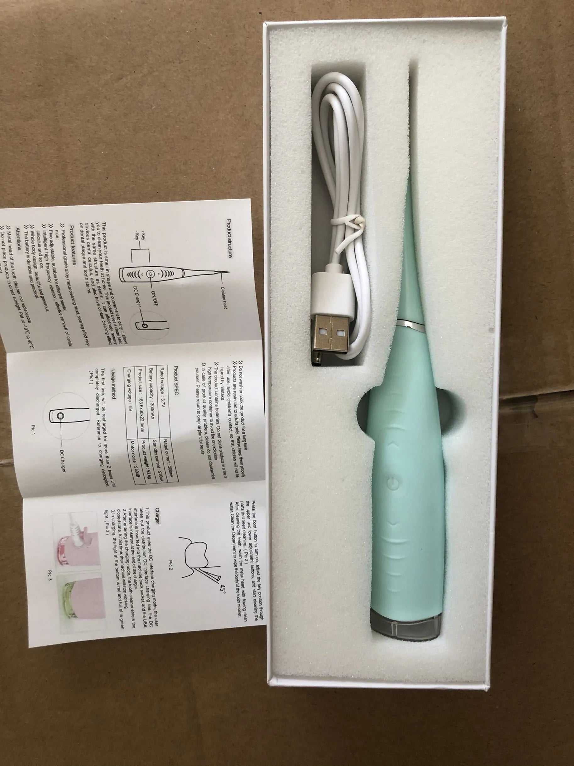 Pink and blue waterproof electric dental scaler with silicone handle and charging cable on a bathroom counter.