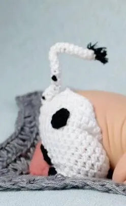 Hand-knitted white baby cow suit with hat and trousers for a newborn.