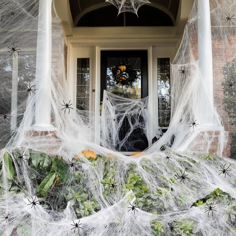 White cotton spider web Halloween decoration draped with plastic spiders on a dark background.