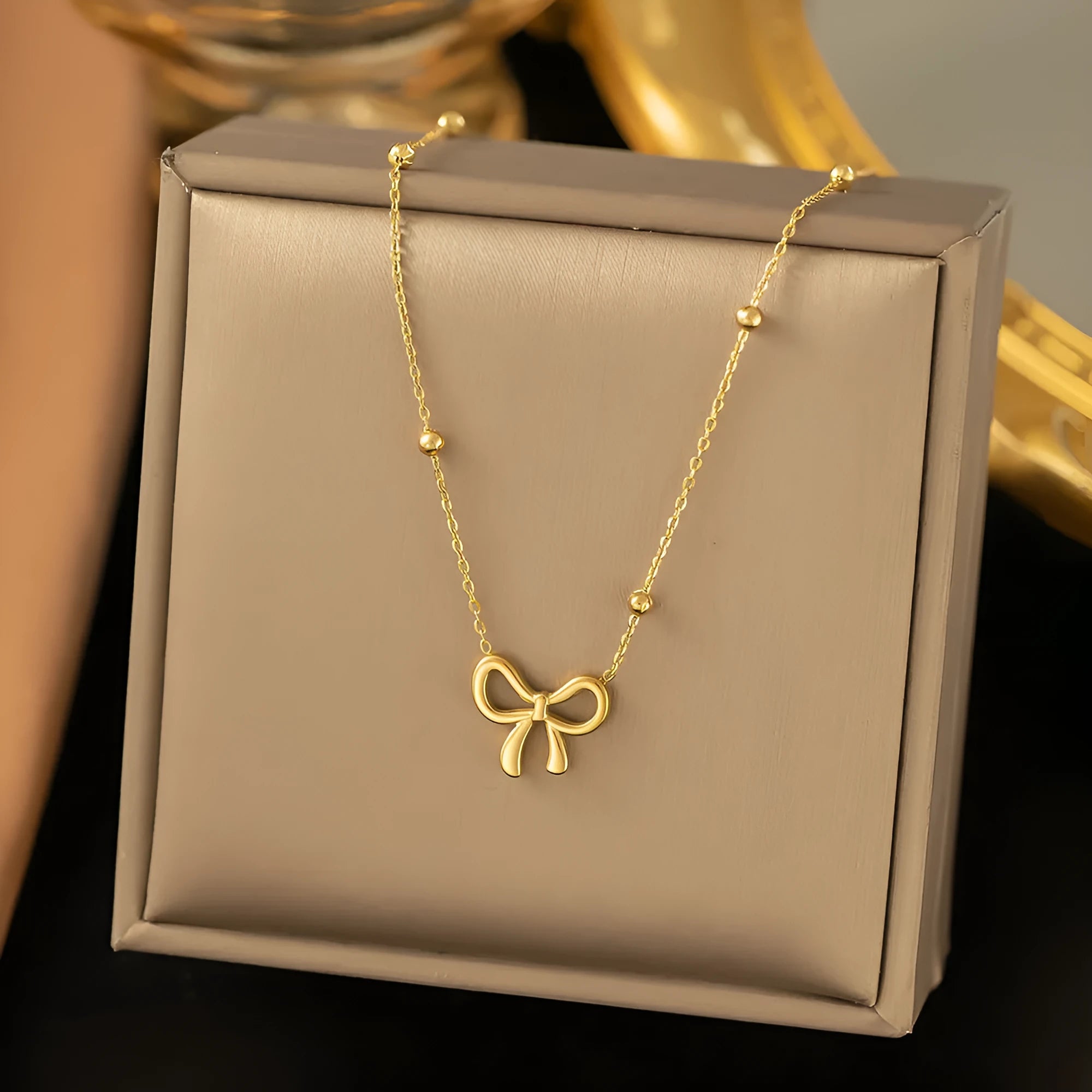Gold electroplated titanium steel bow necklace with cross chain design showing adjustable length mechanism