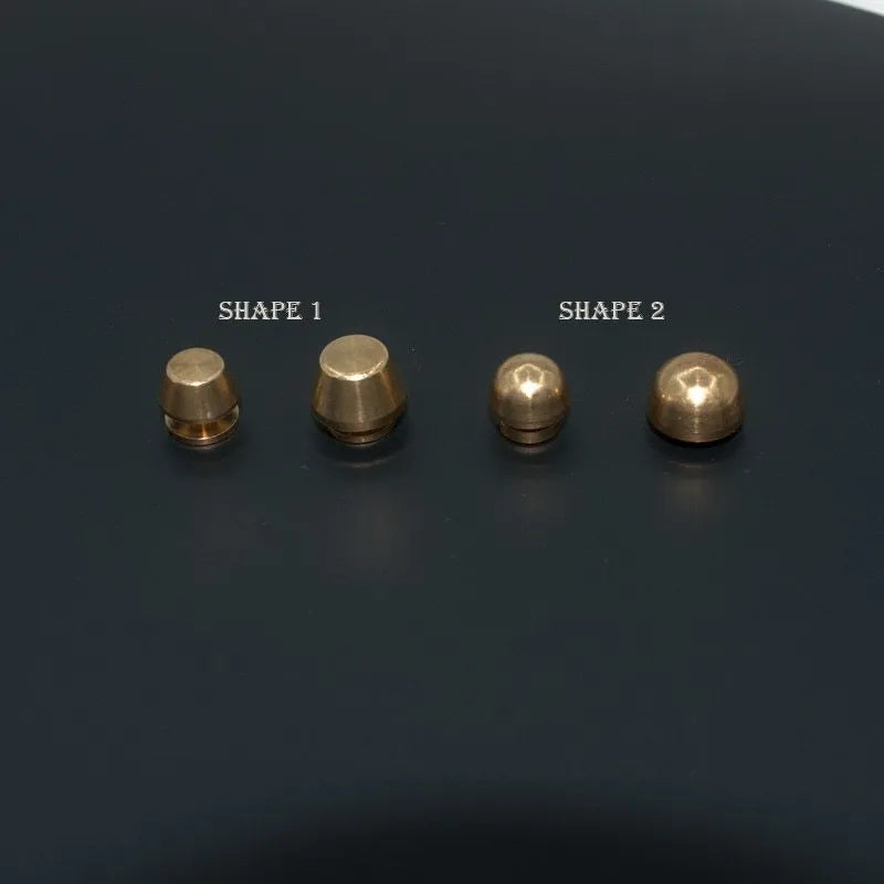 Brass decorative buckle with set of round and bucket-shaped brass foot nails on a surface.