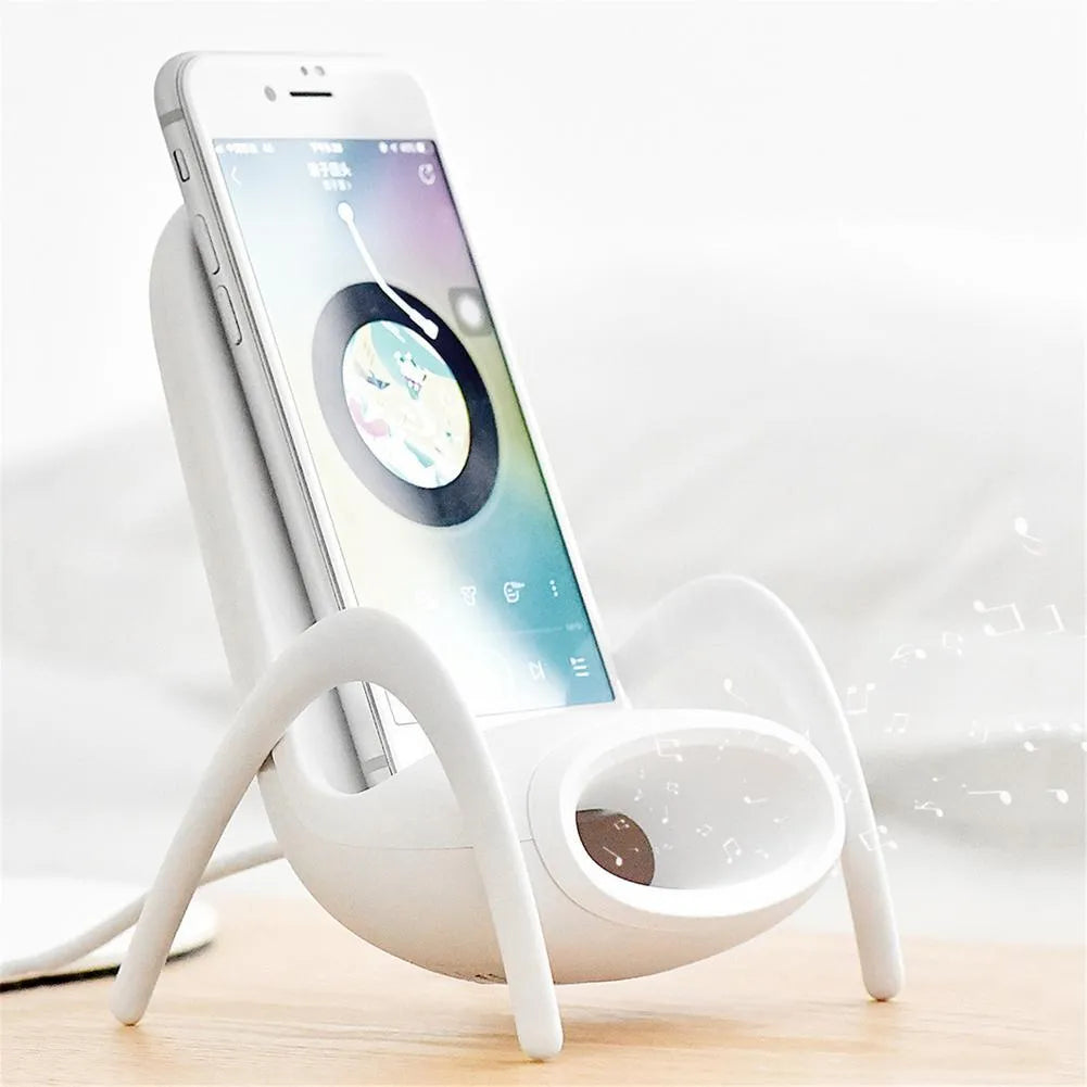 White mini chair shaped wireless charging stand holding a mobile phone on a desk.