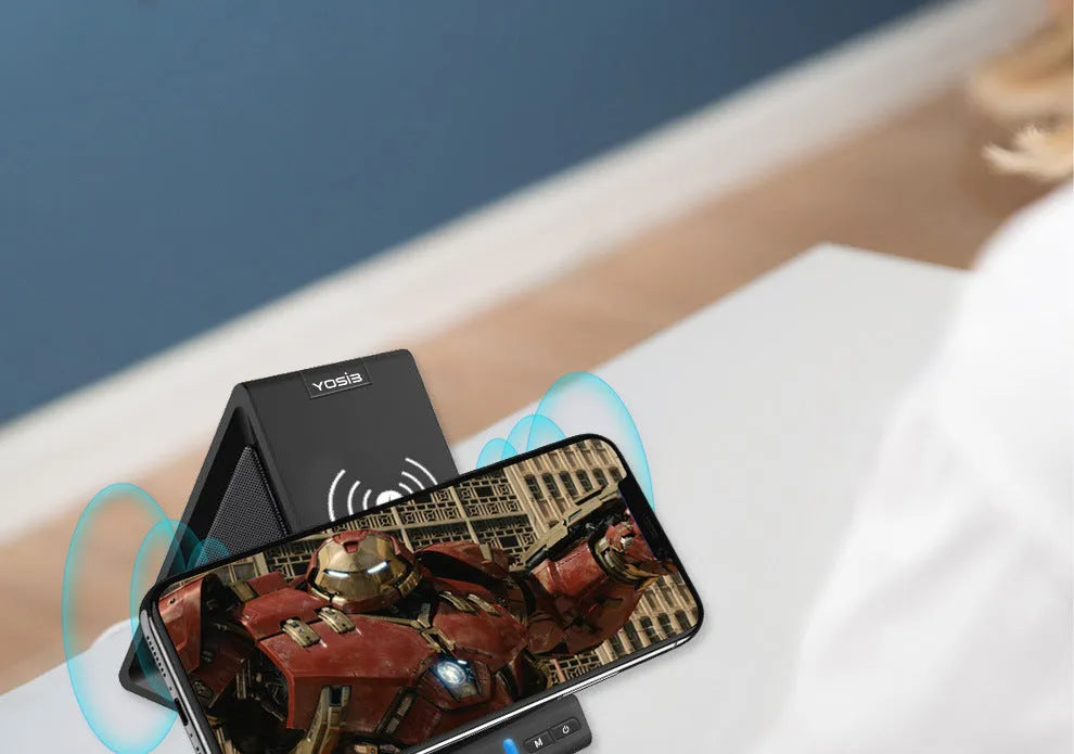 Black multifunctional Bluetooth speaker with integrated phone stand and wireless charging pad on a desk.
