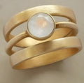 Gold geometric titanium steel ring with a white chalcedony stone inlaid in a hollow design on a finger.