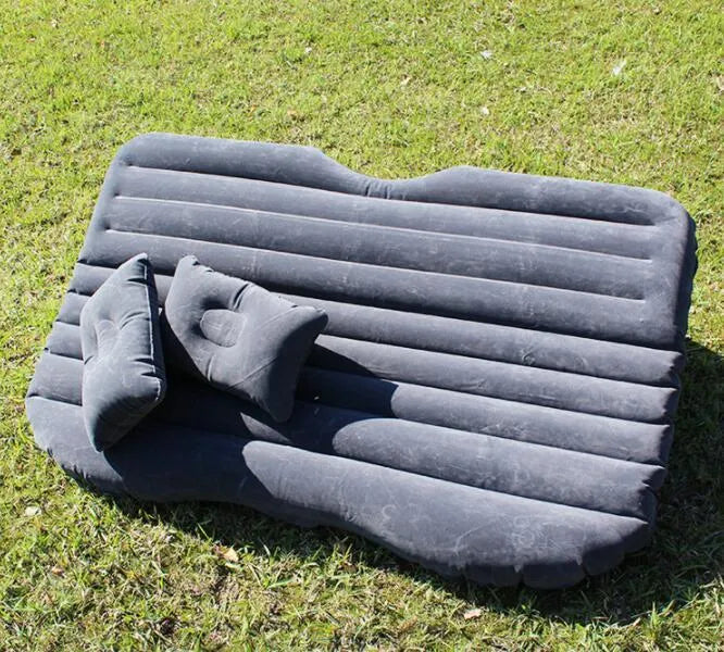 Black inflatable car bed with flocked surface and two pillows, folded next to its storage bag.