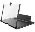 Folding mobile phone screen amplifier in black, with phone inserted, showing 3-4x magnification on a desk