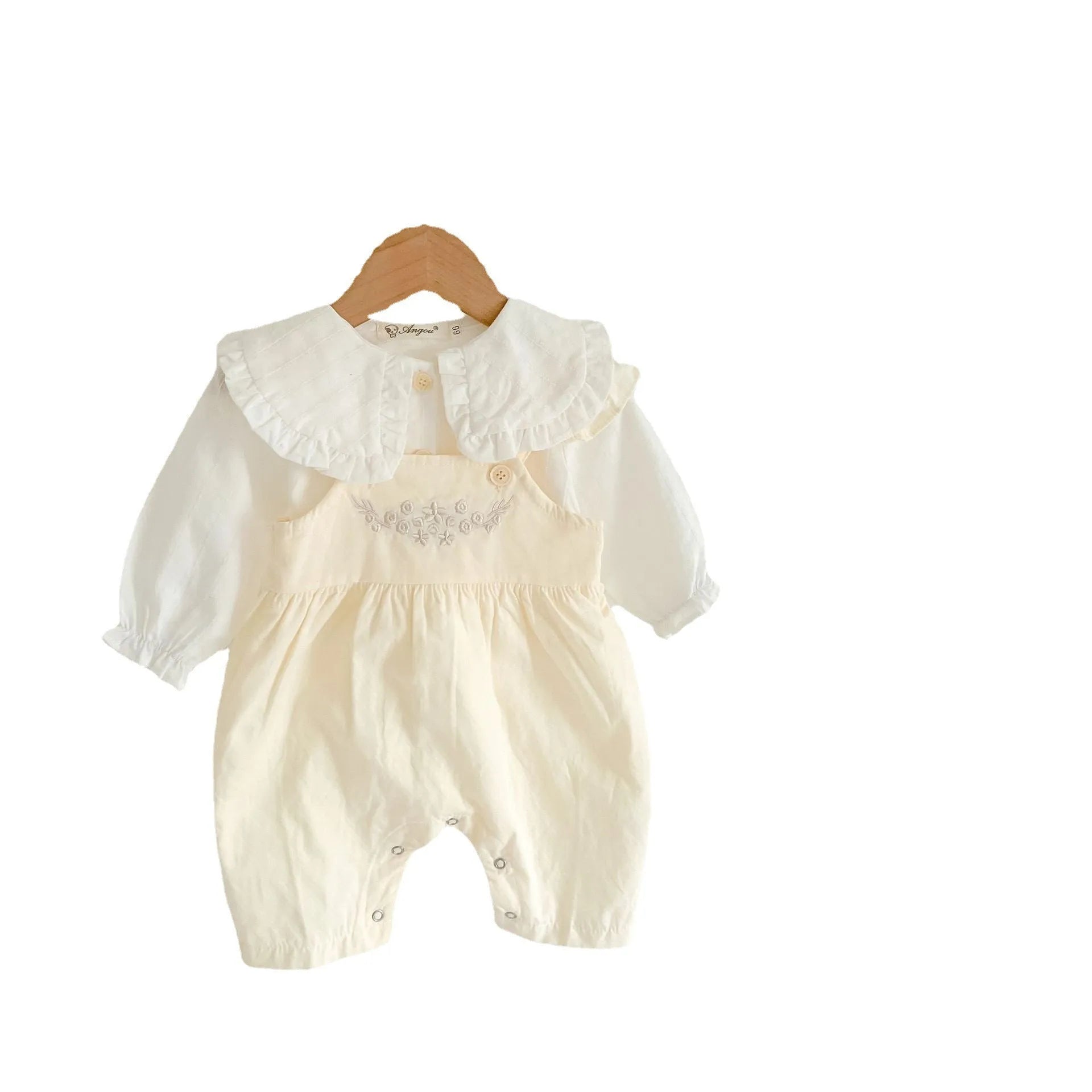 Baby girl wearing a loose-fit cotton suspender romper with adjustable straps in an apricot colour.