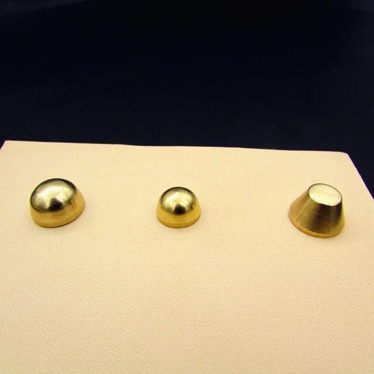 Brass decorative buckle with set of round and bucket-shaped brass foot nails on a surface.