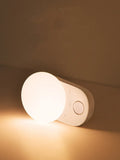 White Baseus rechargeable sensor night light with LED glow, shown on a bedside table.
