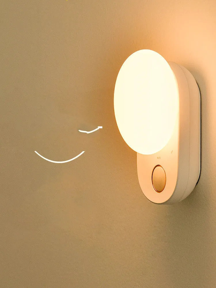 White Baseus rechargeable sensor night light with LED glow, shown on a bedside table.