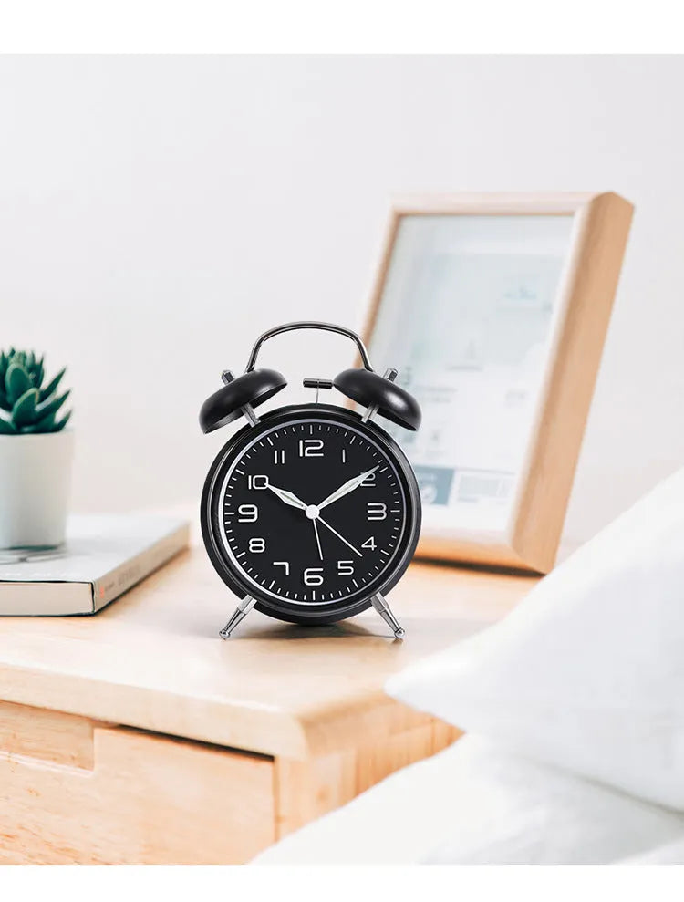 Large black metal alarm clock with luminous hands and 4-inch glass dial on a bedside table