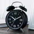 Large black metal alarm clock with luminous hands and 4-inch glass dial on a bedside table