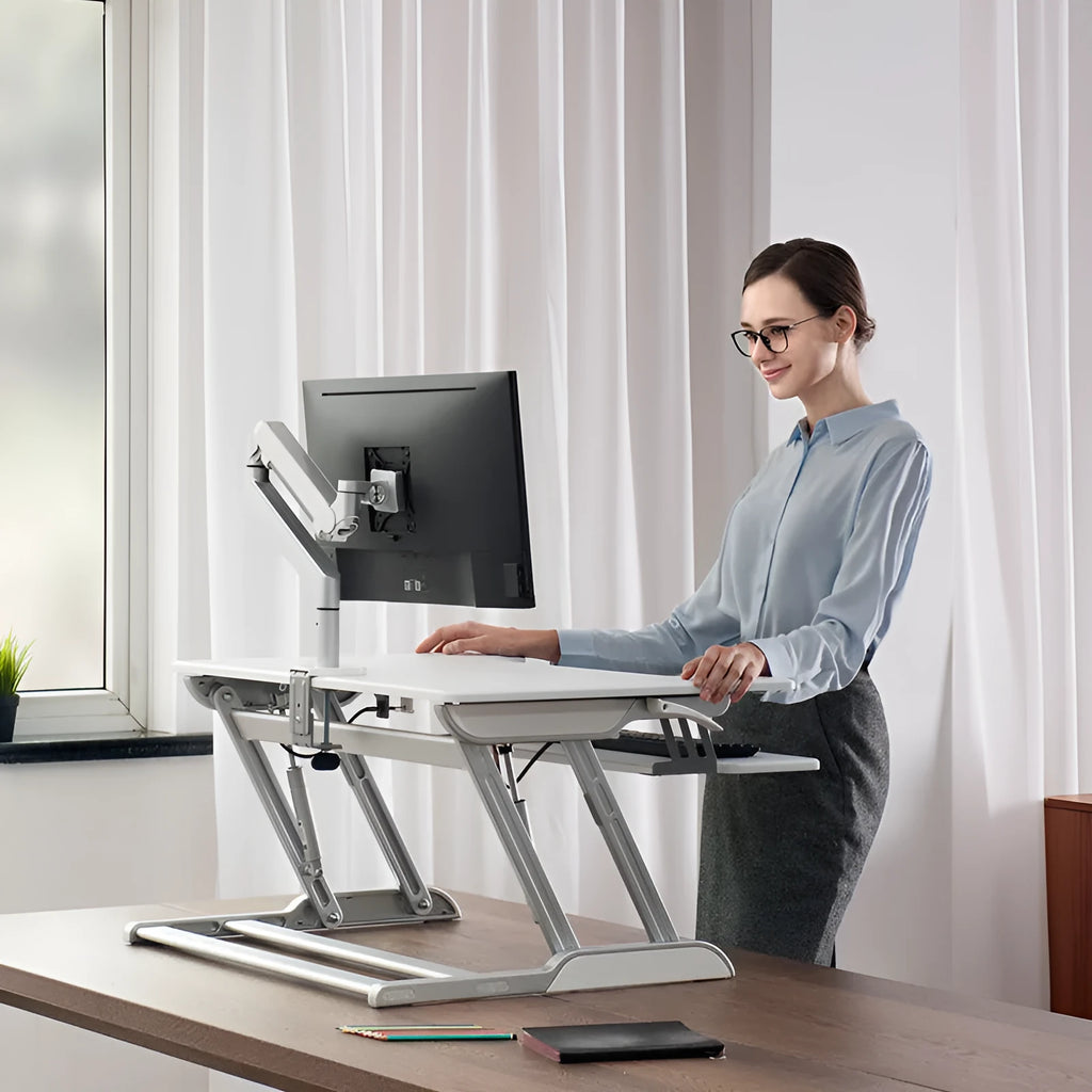 Adjustable lifting computer stand in dark grey supporting a monitor on a desk