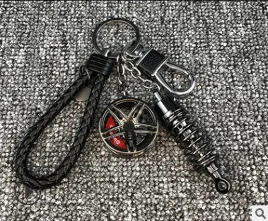 Silver metal wheel and shock absorber keychain with black braided rope and waist buckle on a white surface