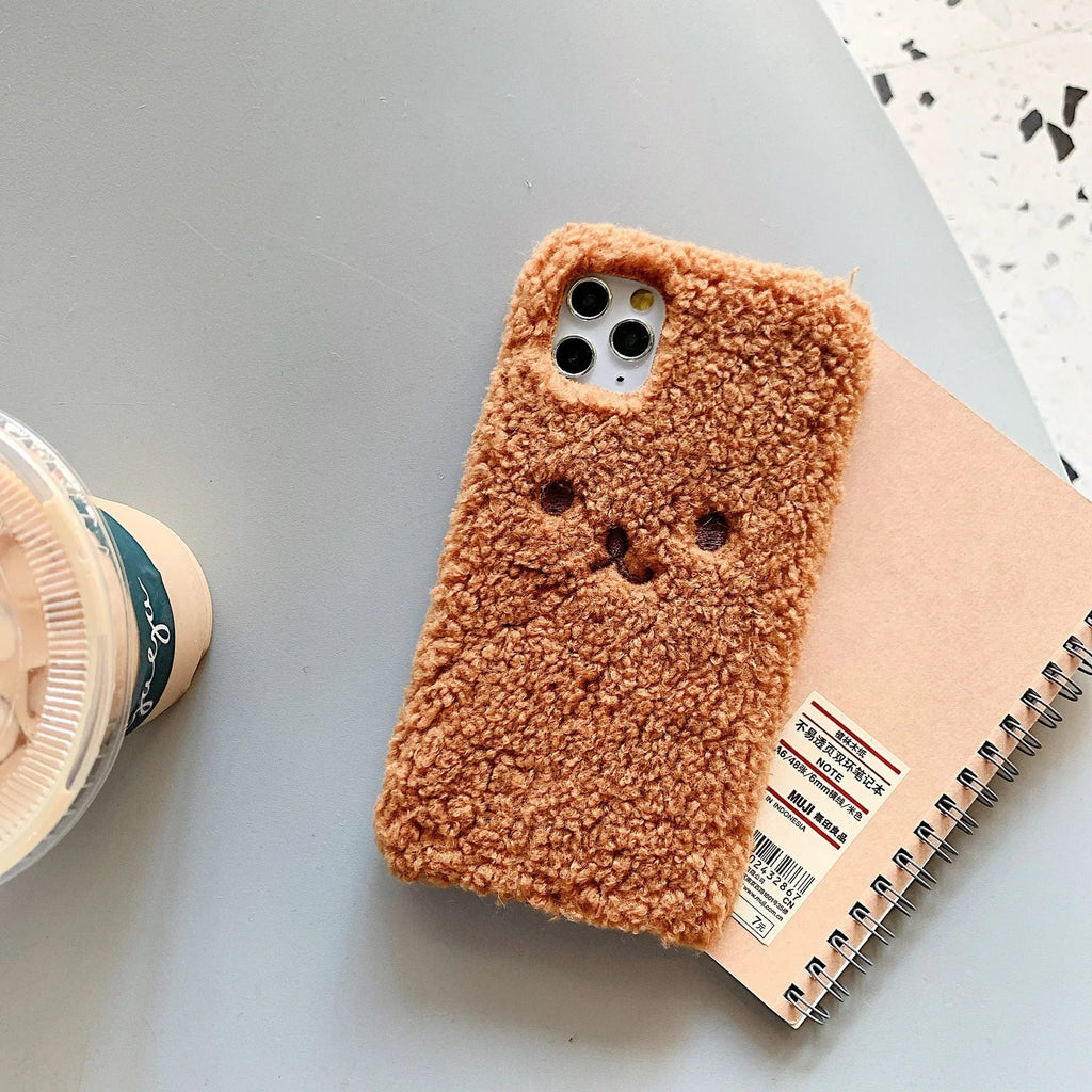 Brown embroidered plush bear face on a flexible TPU iPhone case, showing raised edges and precise button cutouts.