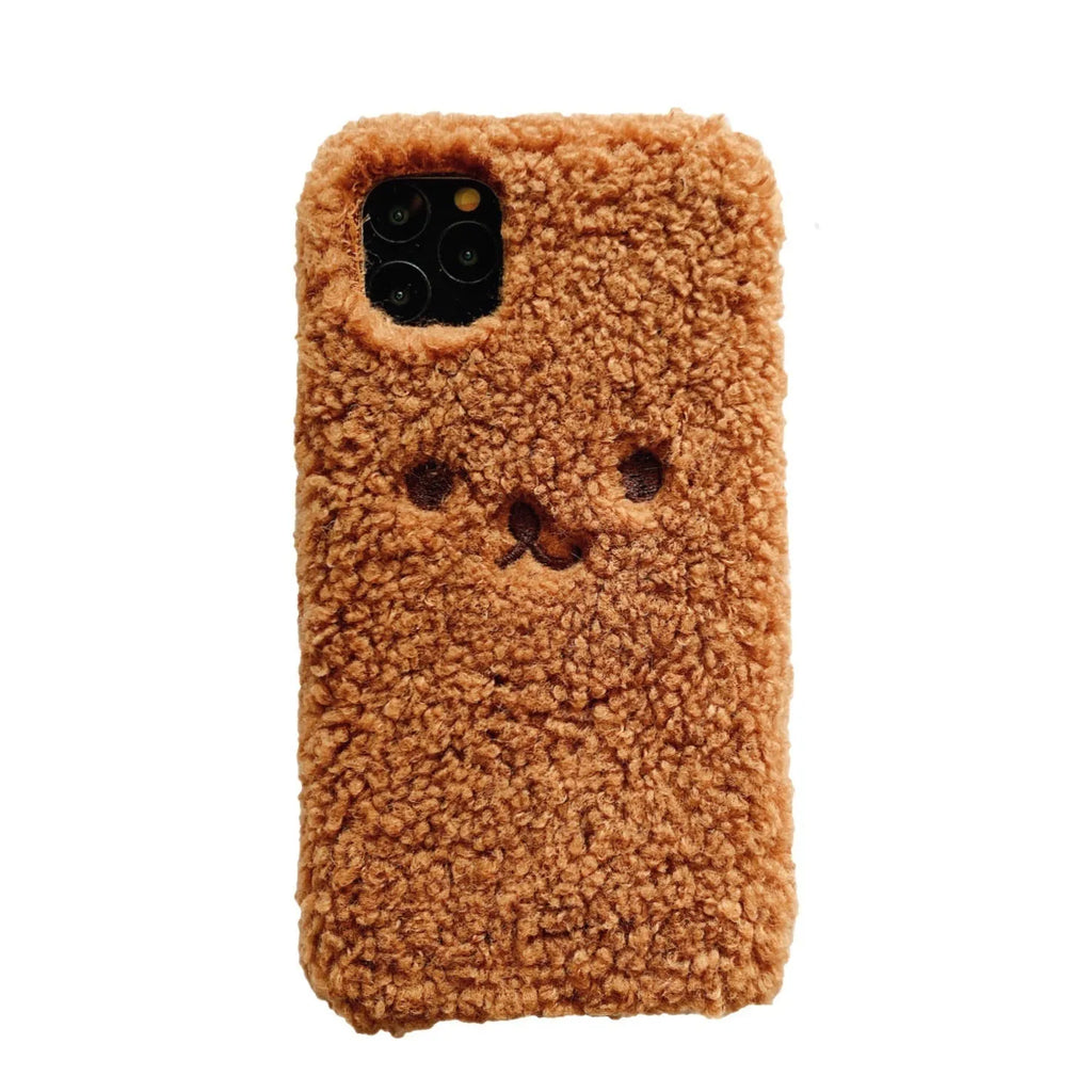 Brown embroidered plush bear face on a flexible TPU iPhone case, showing raised edges and precise button cutouts.