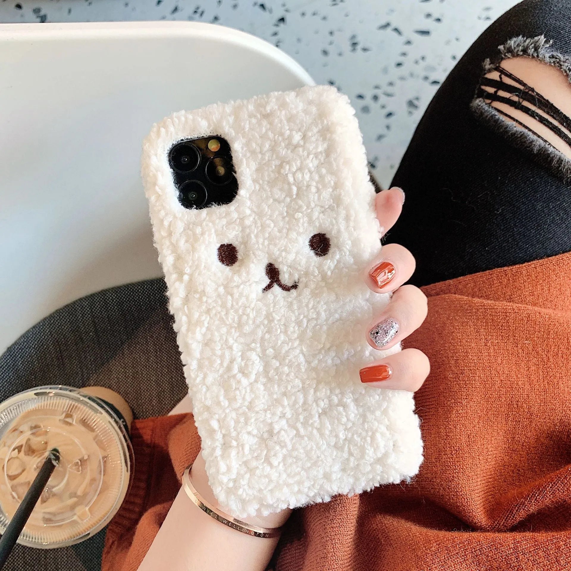 Brown embroidered plush bear face on a flexible TPU iPhone case, showing raised edges and precise button cutouts.
