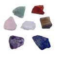 Seven natural white crystal rough stones in rainbow chakra colours on a flat surface