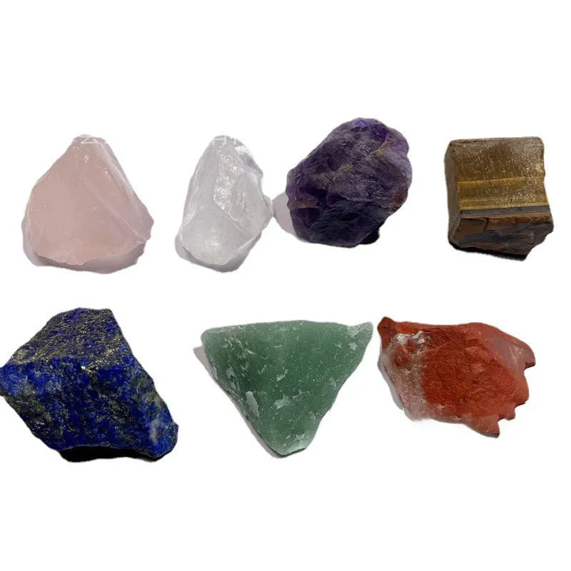 Seven natural white crystal rough stones in rainbow chakra colours on a flat surface